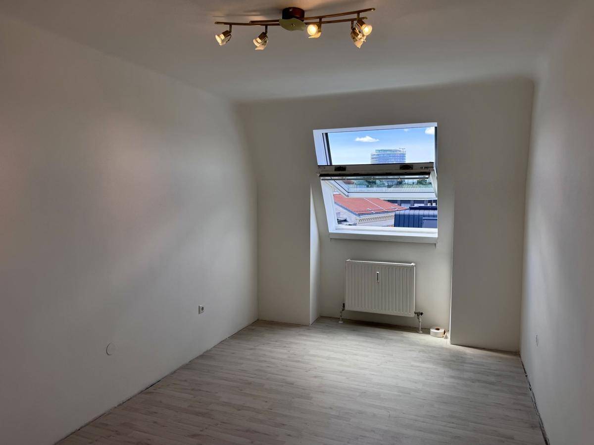 Schlafzimmer mit hellem Laminatboden, Dachfenster und moderner Deckenleuchte.