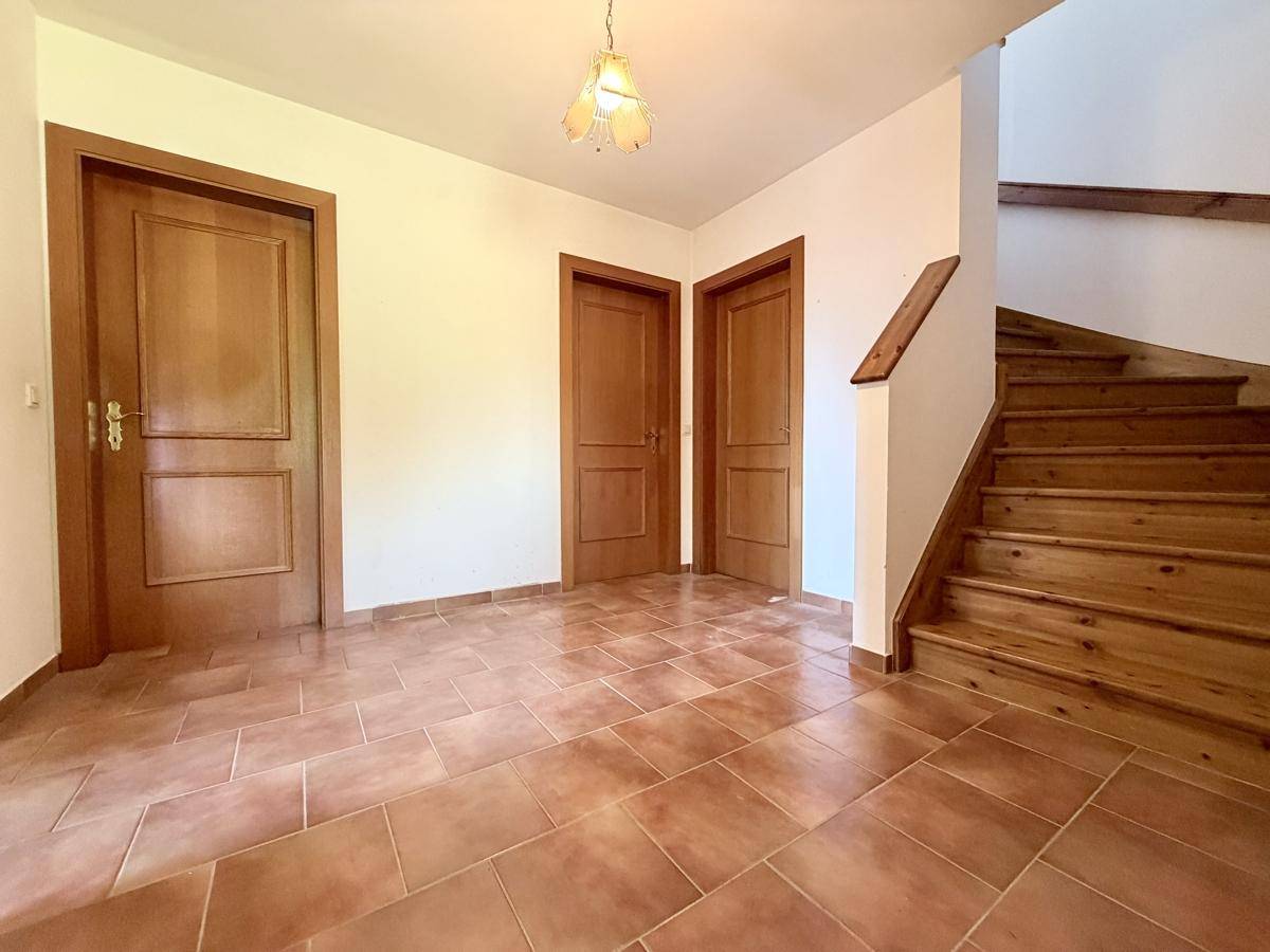 Heller Eingangsbereich mit Terrakotta-Fliesenboden und Holztreppe, die in die oberen Stockwerke führt.