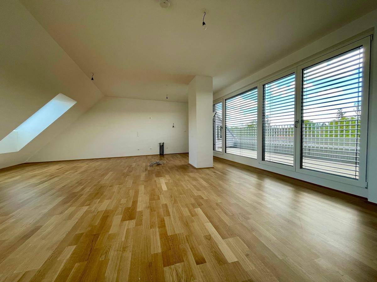 Geräumiger, heller Raum mit Holzparkettboden, großen Fenstern und Zugang zur Terrasse.