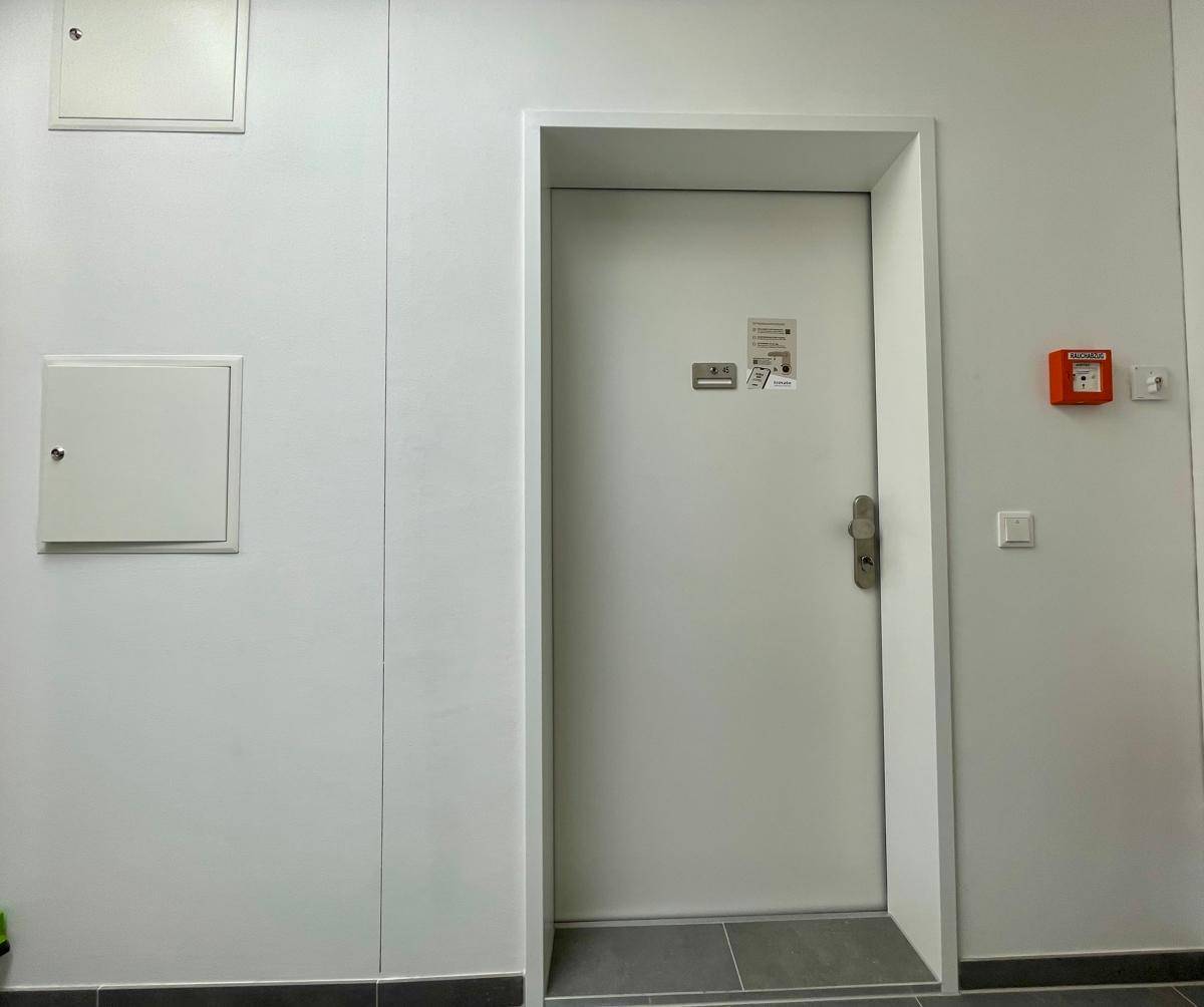 Heller Flur mit weißer Tür, Wandpaneelen und einem Feuermelder.