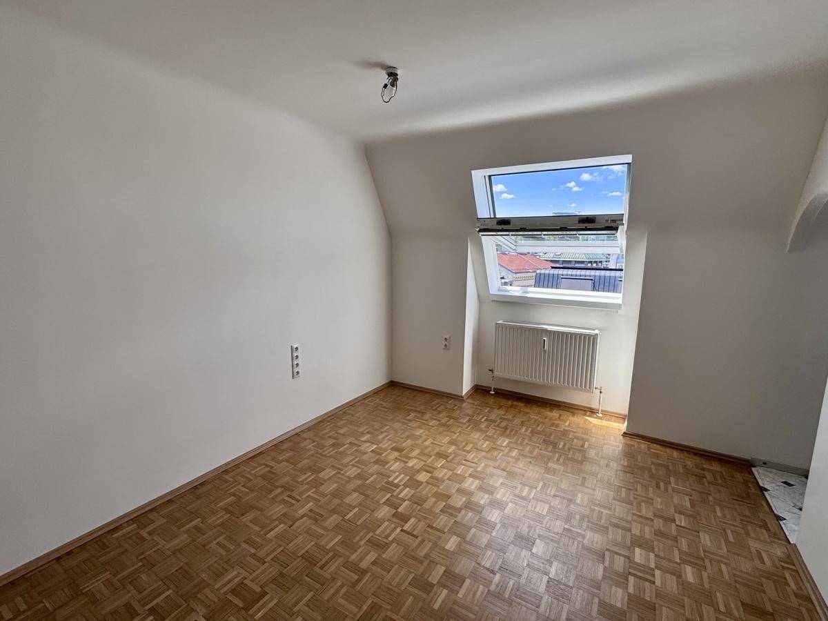 Helles Schlafzimmer mit Parkettboden, Dachfenster und Heizkörper unter dem Fenster.