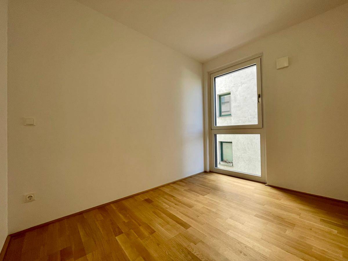 Helles Schlafzimmer mit Parkettboden und einem großen Fenster, das viel Tageslicht bietet.