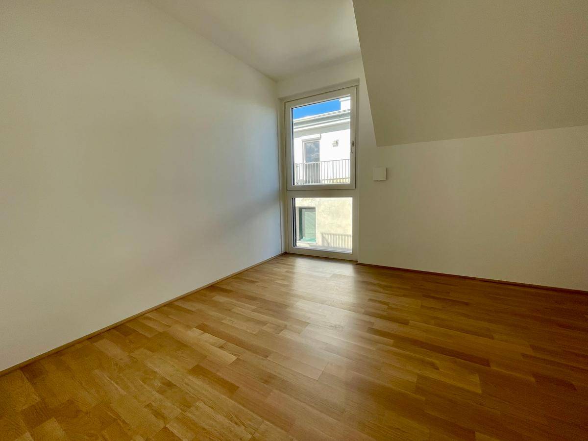 Schlafzimmer mit Holzboden und Fenster, das eine angenehme Helligkeit im Raum schafft.