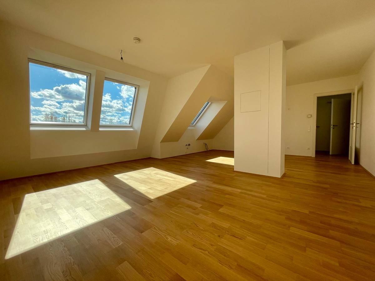 Helles Zimmer im Dachgeschoss mit Parkettboden, Dachschräge und mehreren Fenstern.