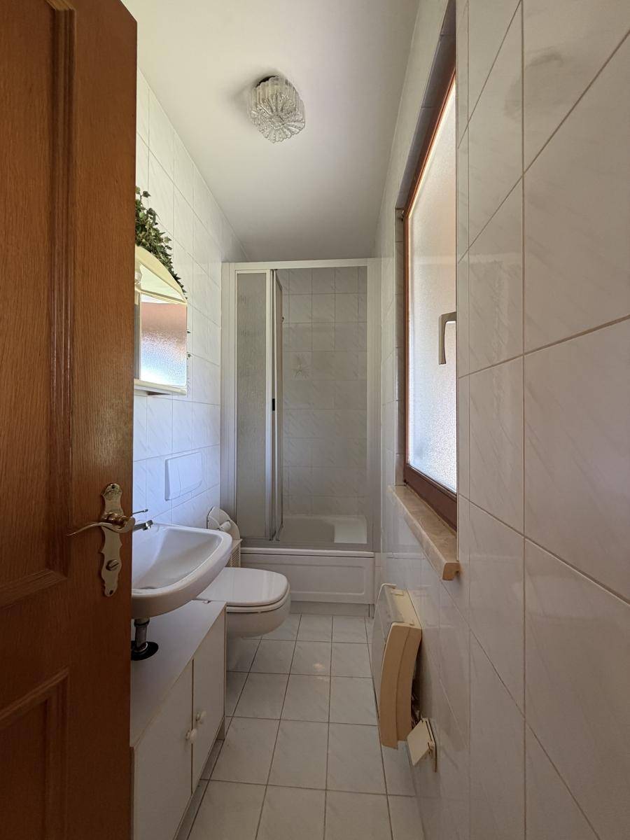 Kleines Badezimmer mit Dusche, WC und Waschbecken, komplett gefliest und mit Fenster.