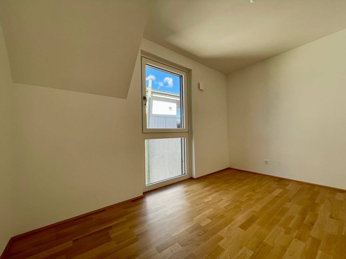 Helles Schlafzimmer mit Holzboden und großem Fenster, das viel Tageslicht in den Raum bringt.