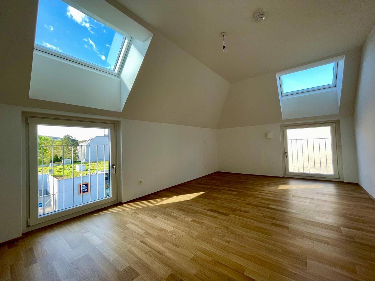 Heller Wohnraum mit Holzparkett, Dachschrägen und großen Dachfenstern, der viel Licht hereinlässt.