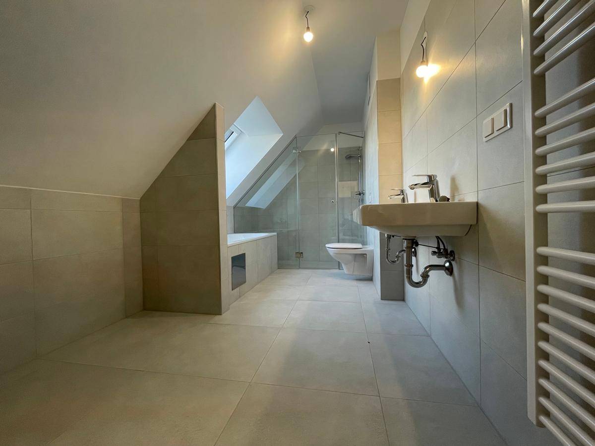 Modernes Badezimmer mit Dachschräge, hellen Fliesen, Dusche, Badewanne und beheiztem Handtuchhalter.