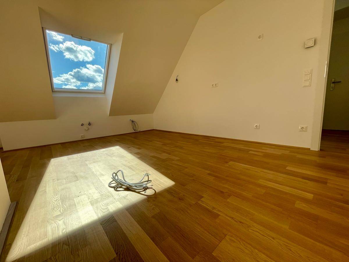 Dachgeschosszimmer mit Parkettboden, Dachschräge und einem hellen Dachfenster.
