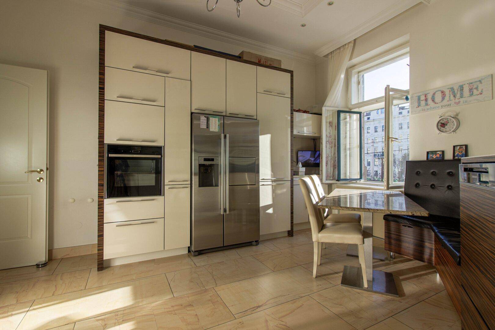 Funktionale Küche mit integriertem Kühlschrank, Backofen und einem kleinen Essbereich am Fenster.