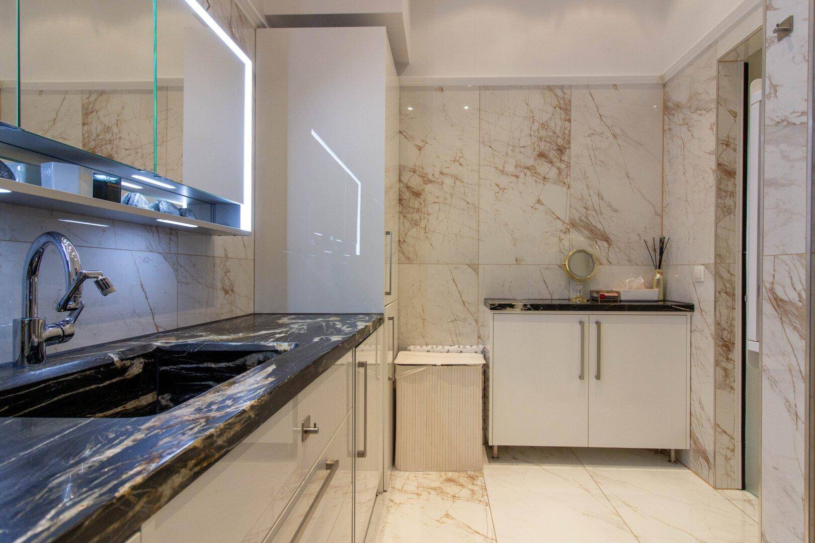 Luxuriöses Badezimmer mit Marmorfliesen, schwarzer Granitarbeitsplatte und eleganten Armaturen.