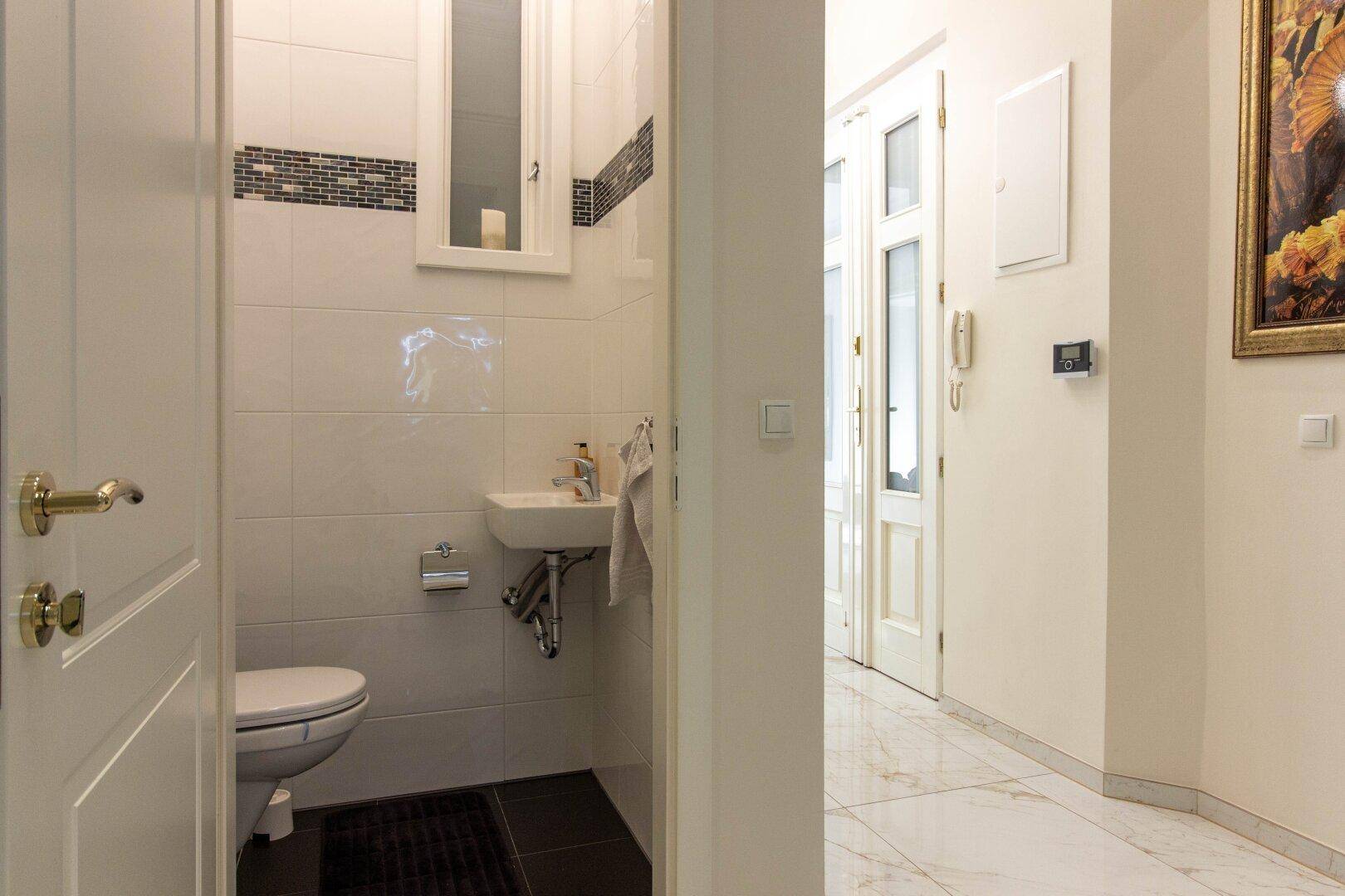 Kleines Gäste-WC mit Fenster, weißen Fliesen und einem kompakten Waschbecken.