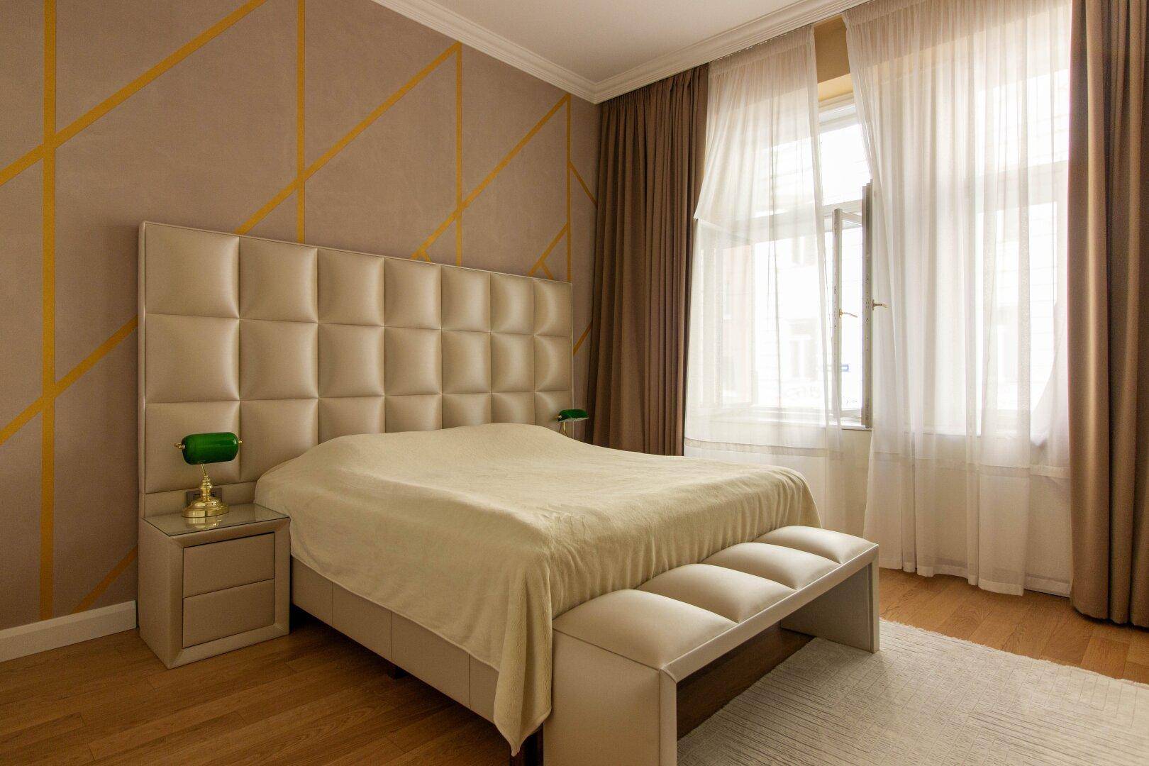 Elegantes Schlafzimmer mit gepolstertem Kopfteil, Parkettboden und dekorativer Wandgestaltung.