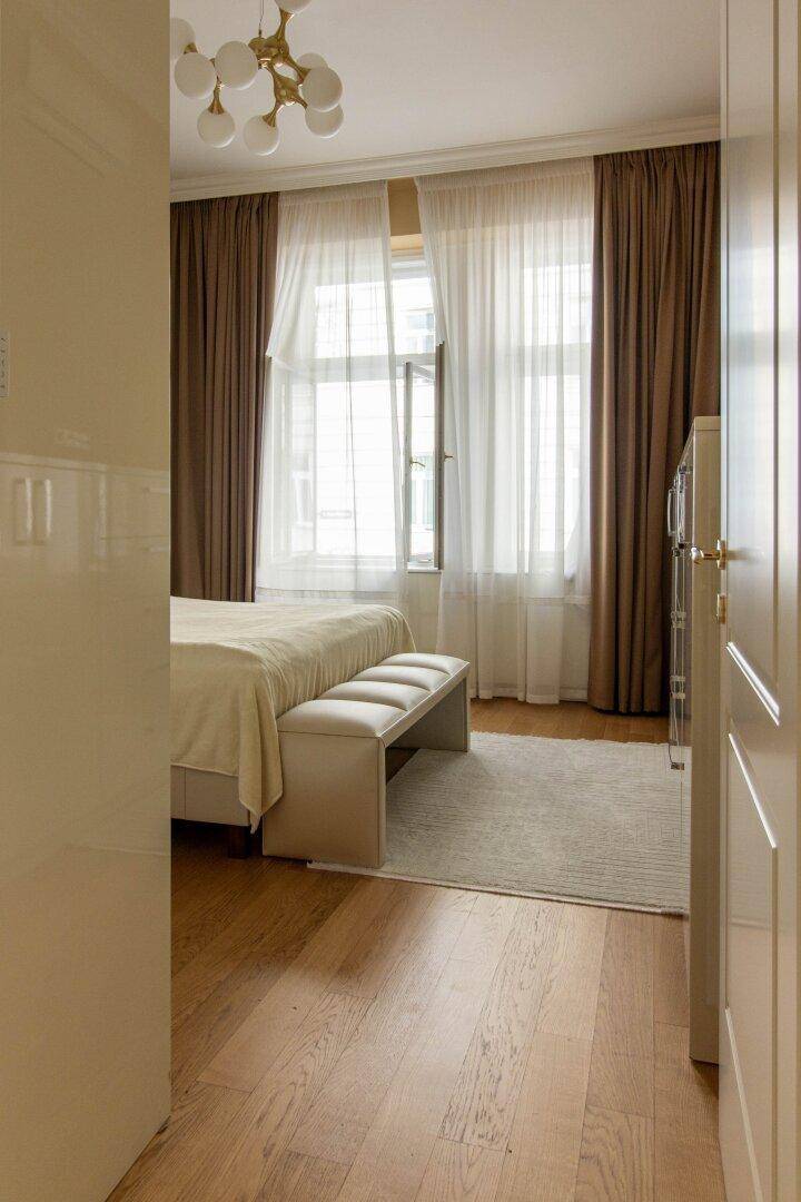 Schlafzimmer mit Parkettboden, großen Fenstern und hellen Vorhängen, die viel Licht hereinlassen.
