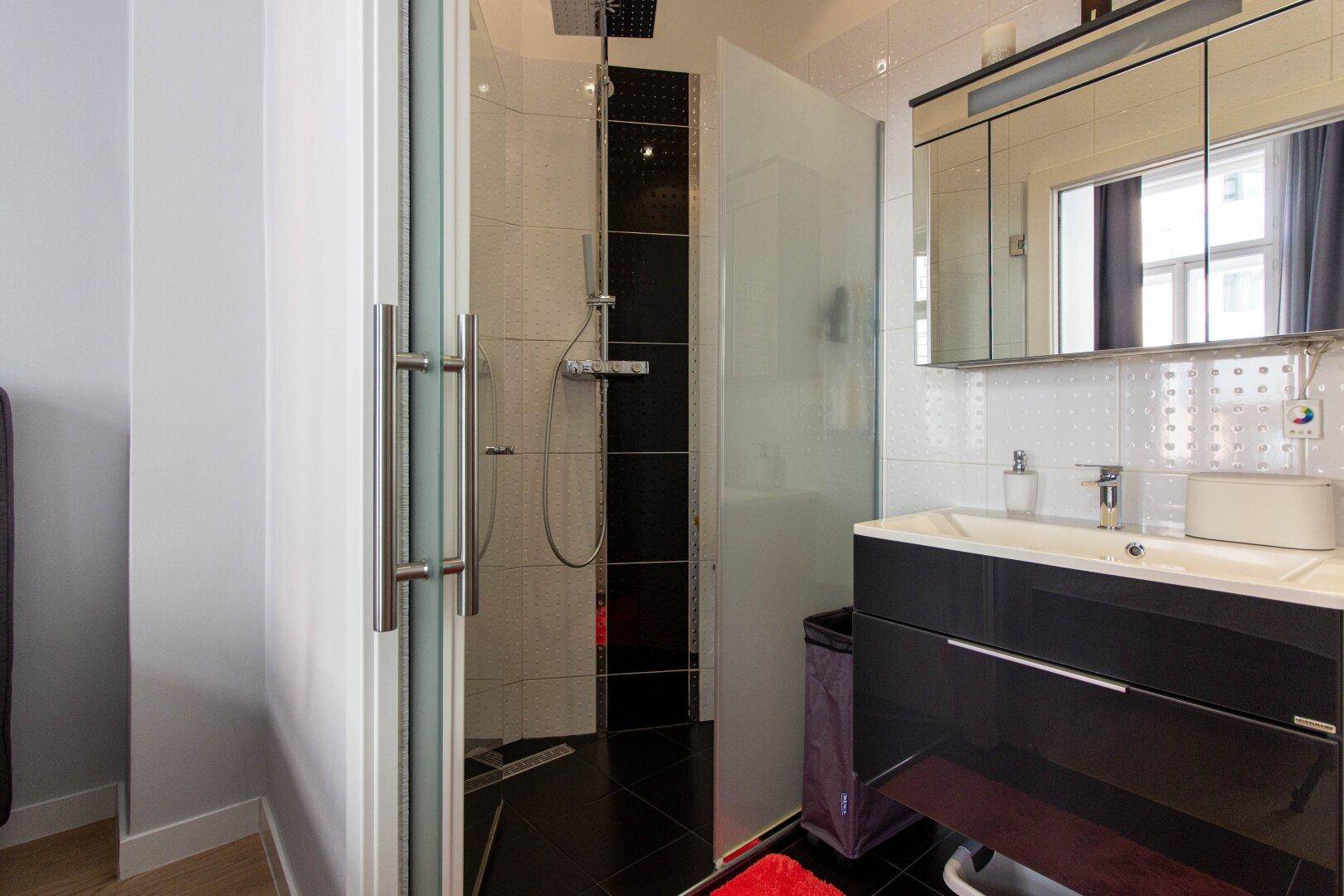 Modernes Badezimmer mit begehbarer Dusche, dunklen Fliesen und Spiegelschrank über dem Waschbecken.