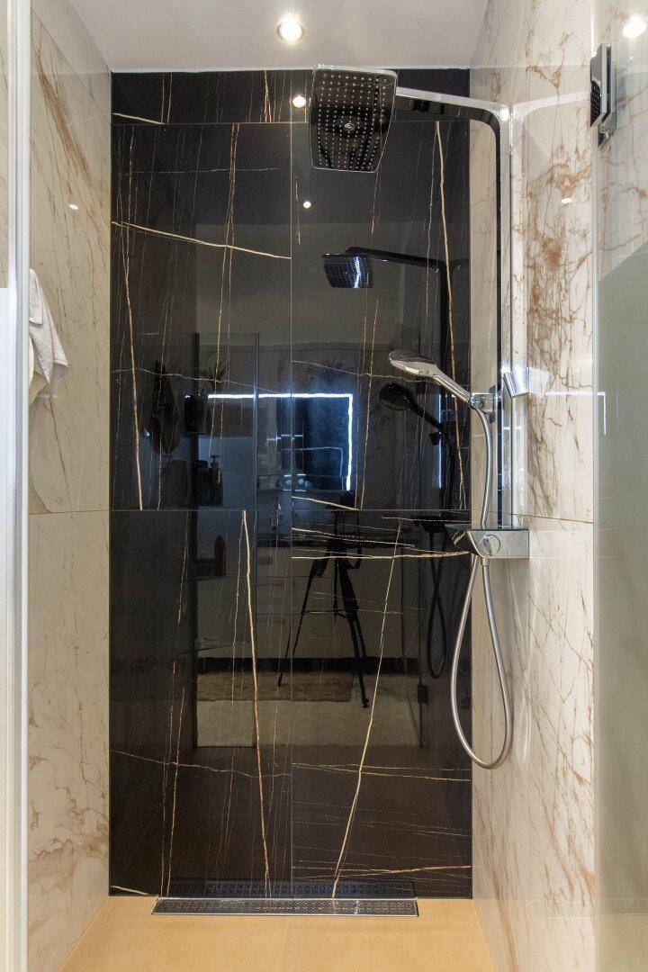 Elegante Dusche mit schwarzen Marmorfliesen und Regenduschkopf in einem luxuriösen Badezimmer.
