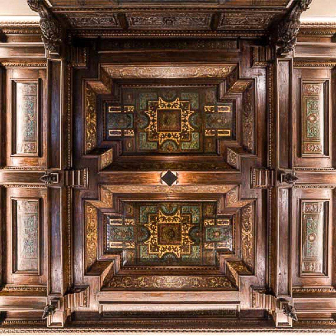 Eine kunstvoll geschnitzte Holzdecke mit aufwendigen Mustern und Verzierungen in dunklen Farbtönen.