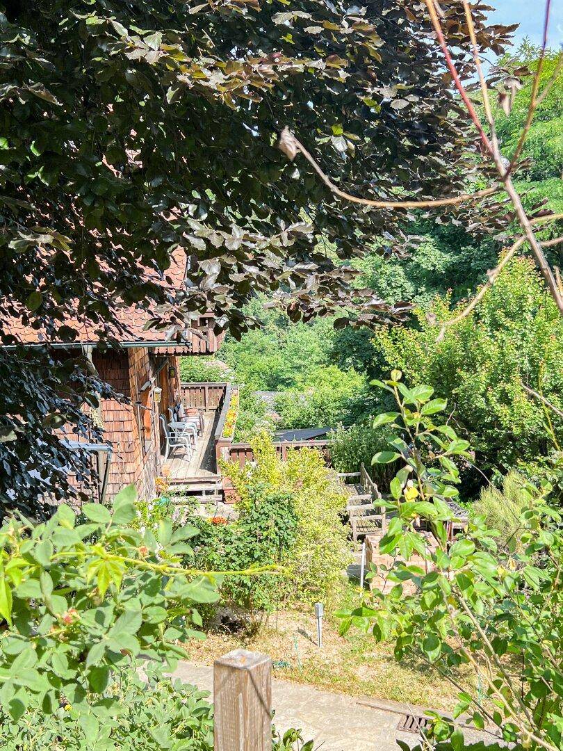 Teilansicht des Hauses, umgeben von üppigem Grün und Bäumen an einem sonnigen Tag.