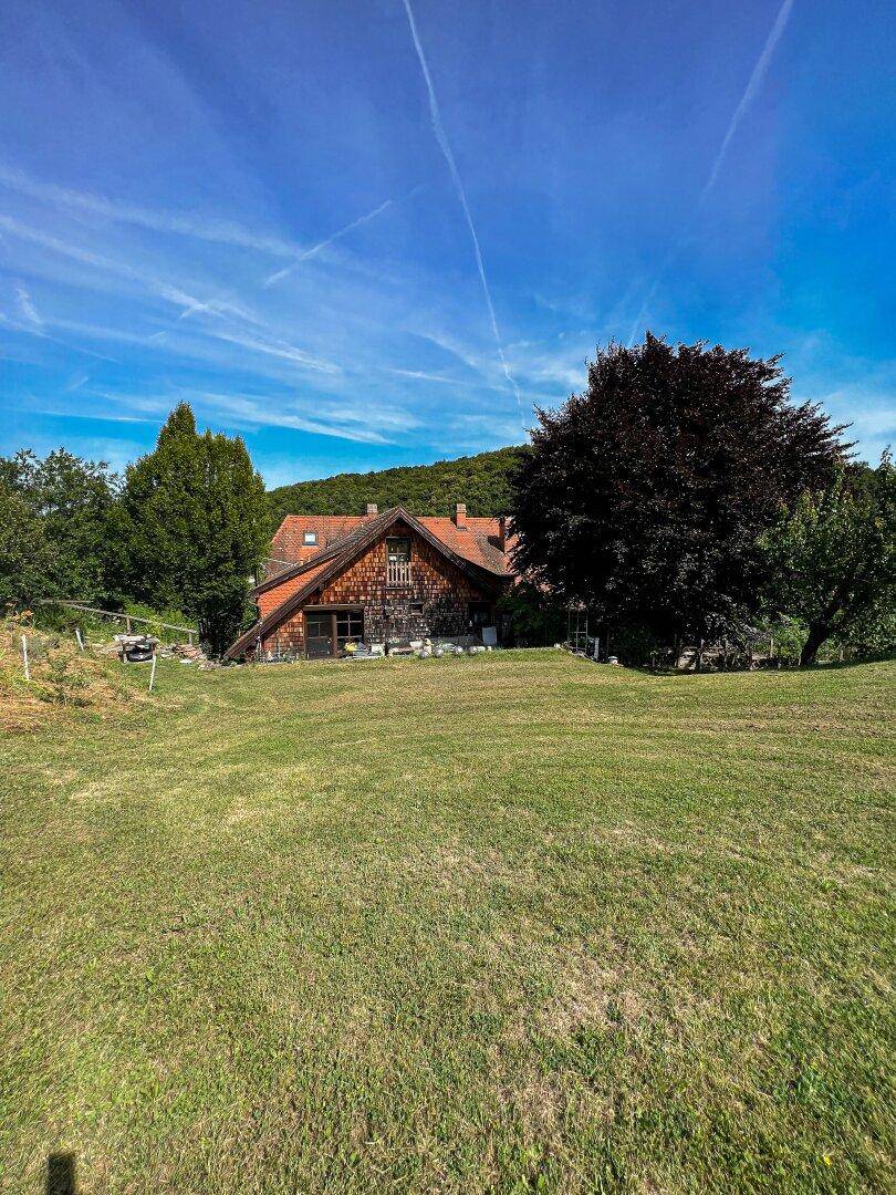 Charmantes Landhaus mit Holzelementen und großem Garten, eingebettet in eine grüne Hügellandschaft.