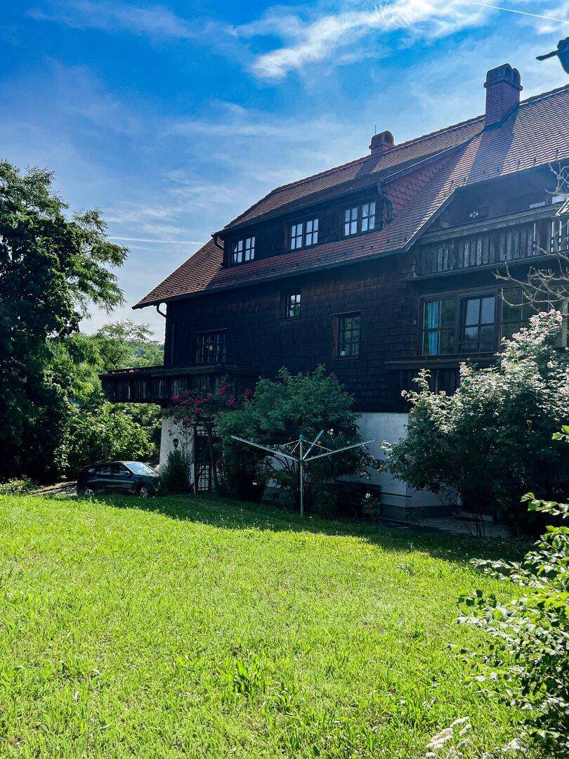 Ansicht des Landhauses mit großem Rasen und üppiger Vegetation unter blauem Himmel.