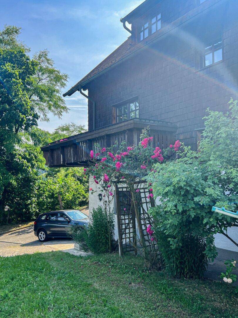 Traditionelles Holzhaus mit blühenden Rosen und üppigem Grün an einem sonnigen Tag.