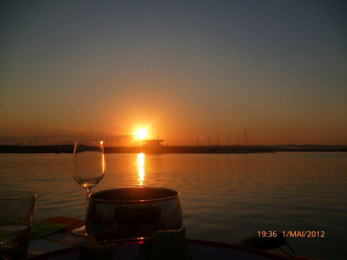 Spektakulärer Sonnenuntergang über dem See, mit einem Weinglas im Vordergrund.