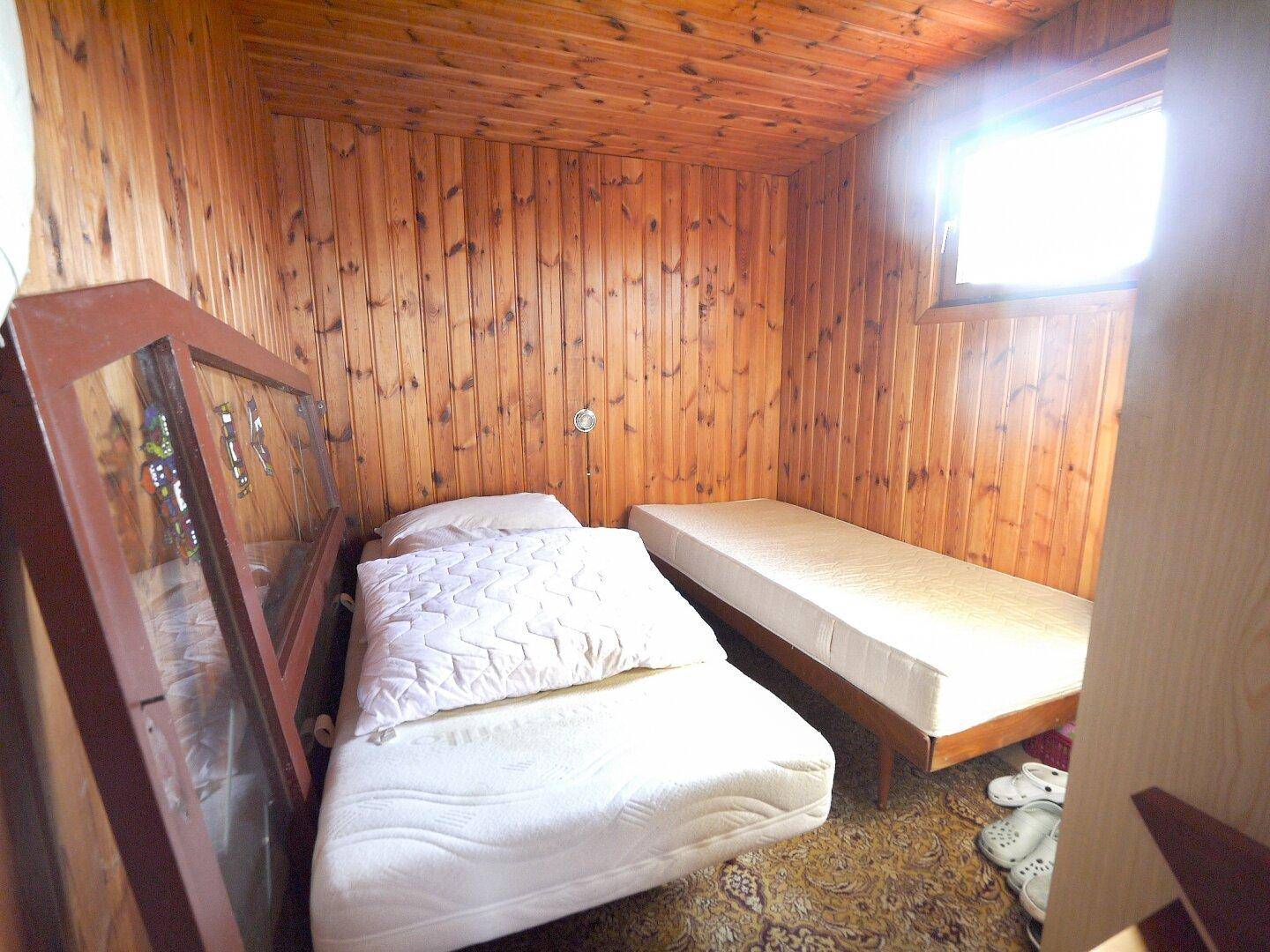 Kleines Schlafzimmer mit Holztäfelung, zwei Einzelbetten und einem Fenster.