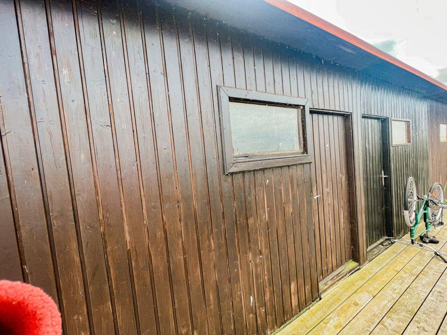 Braune Holzwand eines Gebäudes mit Fenster und Tür, angrenzend an eine Holzterrasse.