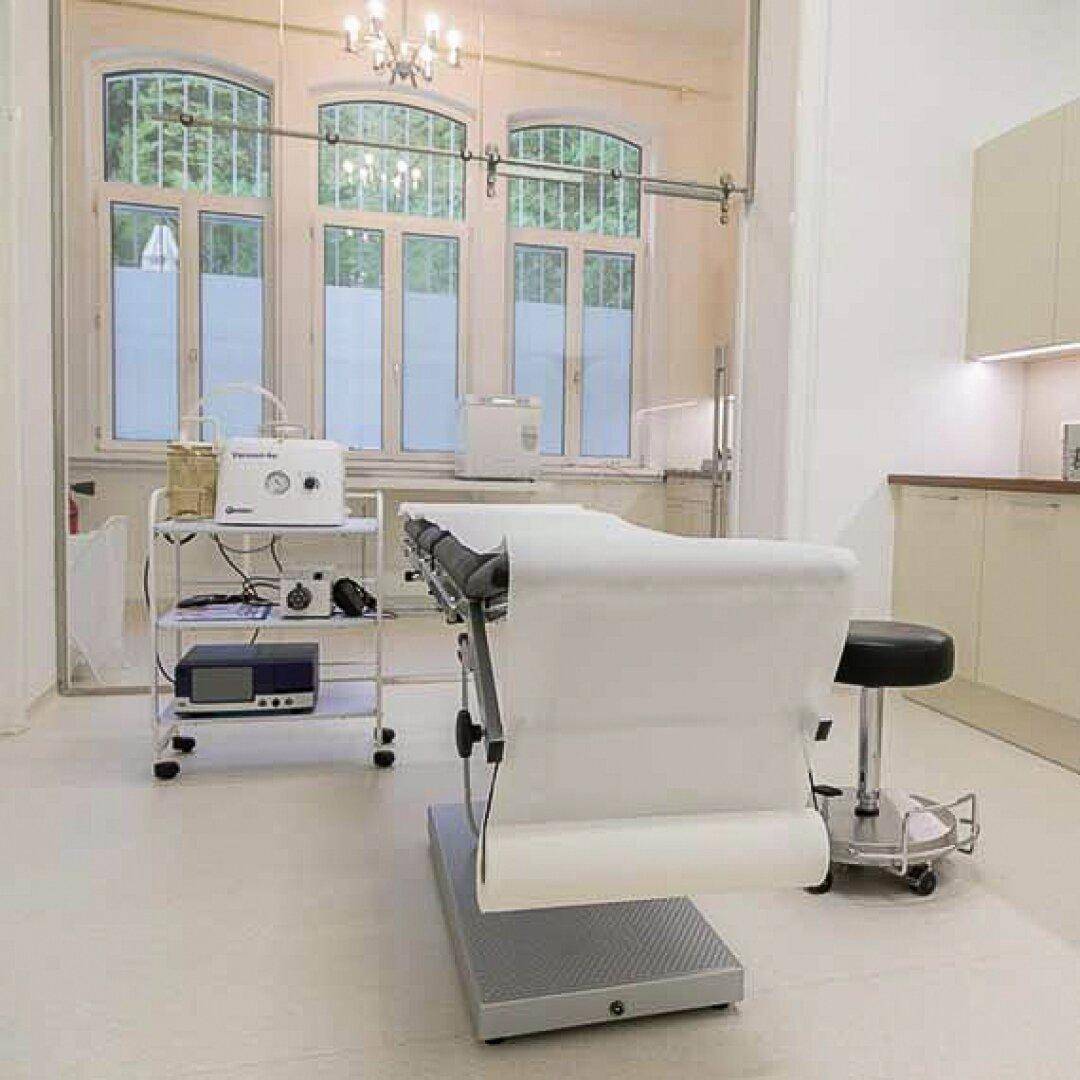 Heller Behandlungsraum mit großen Bogenfenstern, medizinischer Ausstattung und funktionaler Einrichtung.