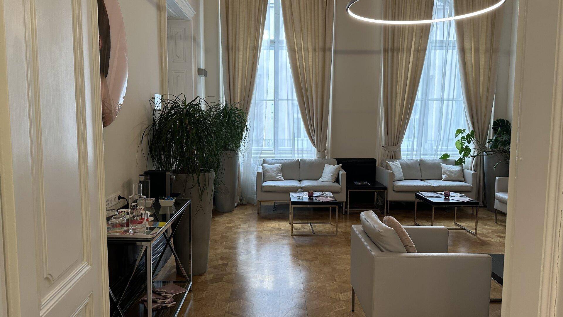 Gemütlicher Wartebereich mit bequemen Sofas, Pflanzen und großen Fenstern.