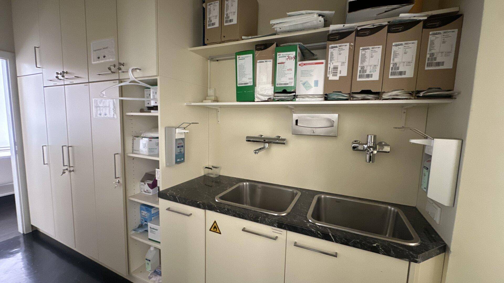Funktionaler Wirtschaftsraum mit zwei Edelstahlspülbecken, dunkler Arbeitsplatte und vielen hellen Schränken für Stauraum.