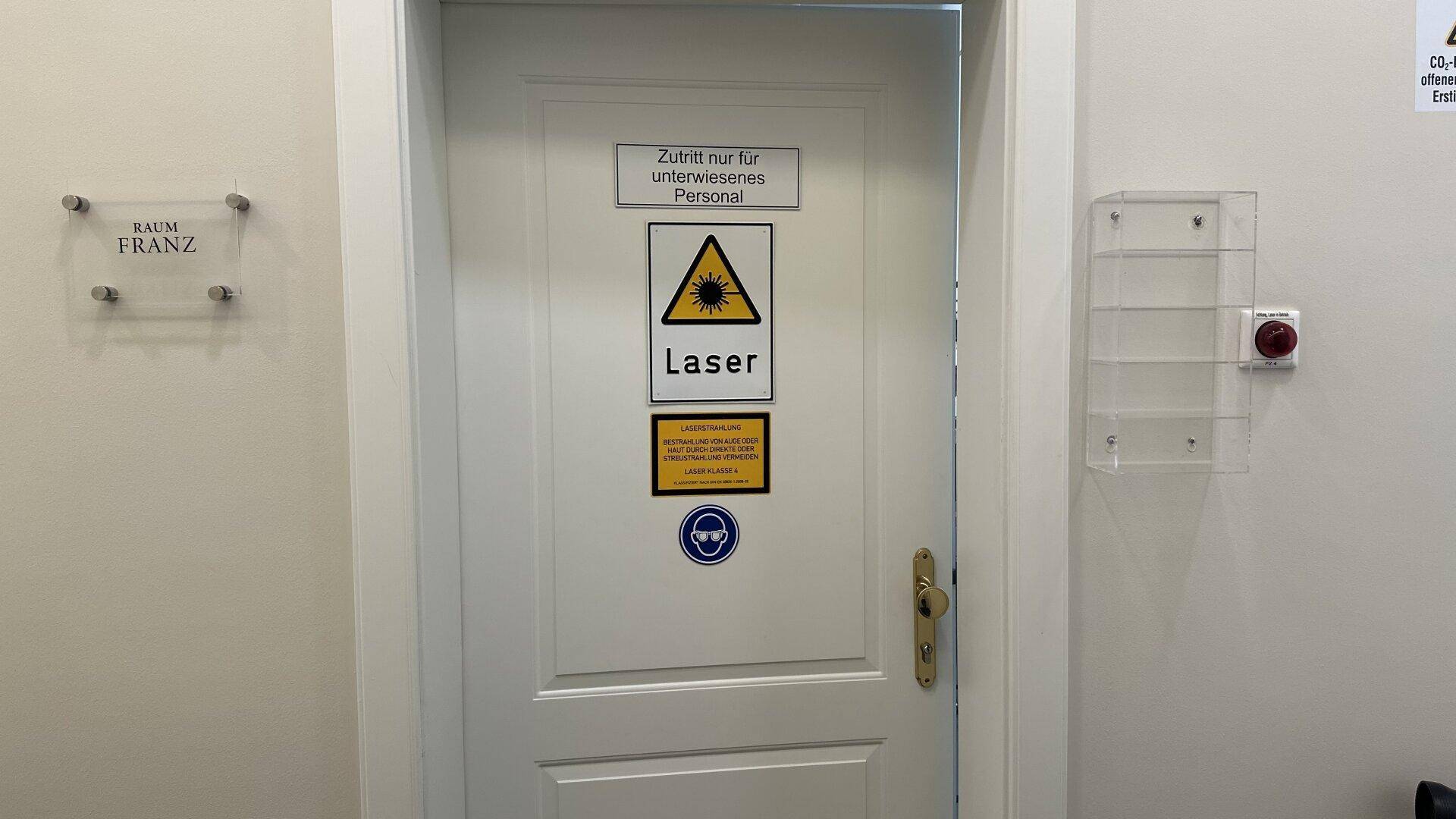 Flur mit einer Tür, die mit Warnschildern für Laserbereich versehen ist.