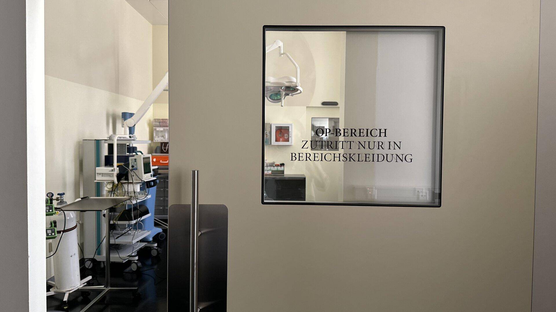 Blick in einen Operationssaal durch ein Fenster mit Hinweisschild.