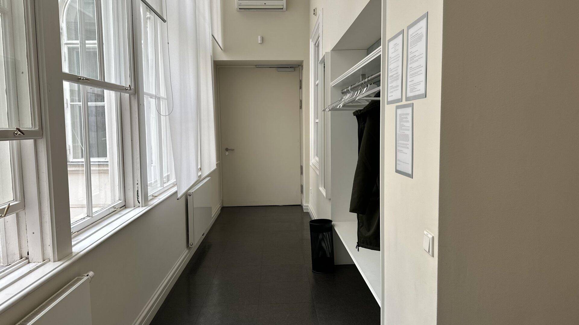 Langer Flur mit großen Fenstern, Garderobe und dunklem Bodenbelag.