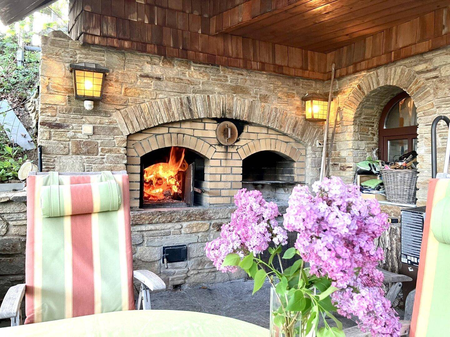 Detailansicht des gemauerten Außenkamins mit brennendem Feuer auf der Terrasse.