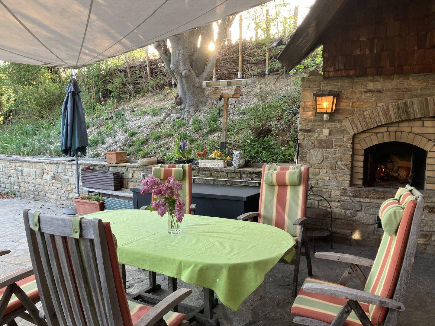 Gemütliche Terrasse mit Steinkamin, Sitzgelegenheiten und Blick ins Grüne.