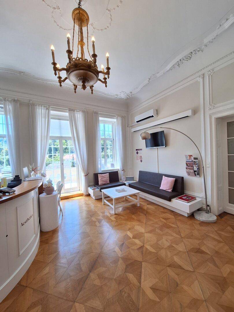 Heller Wartebereich mit bequemen Sofas, Parkettboden und großen Fenstern mit Blick ins Grüne.