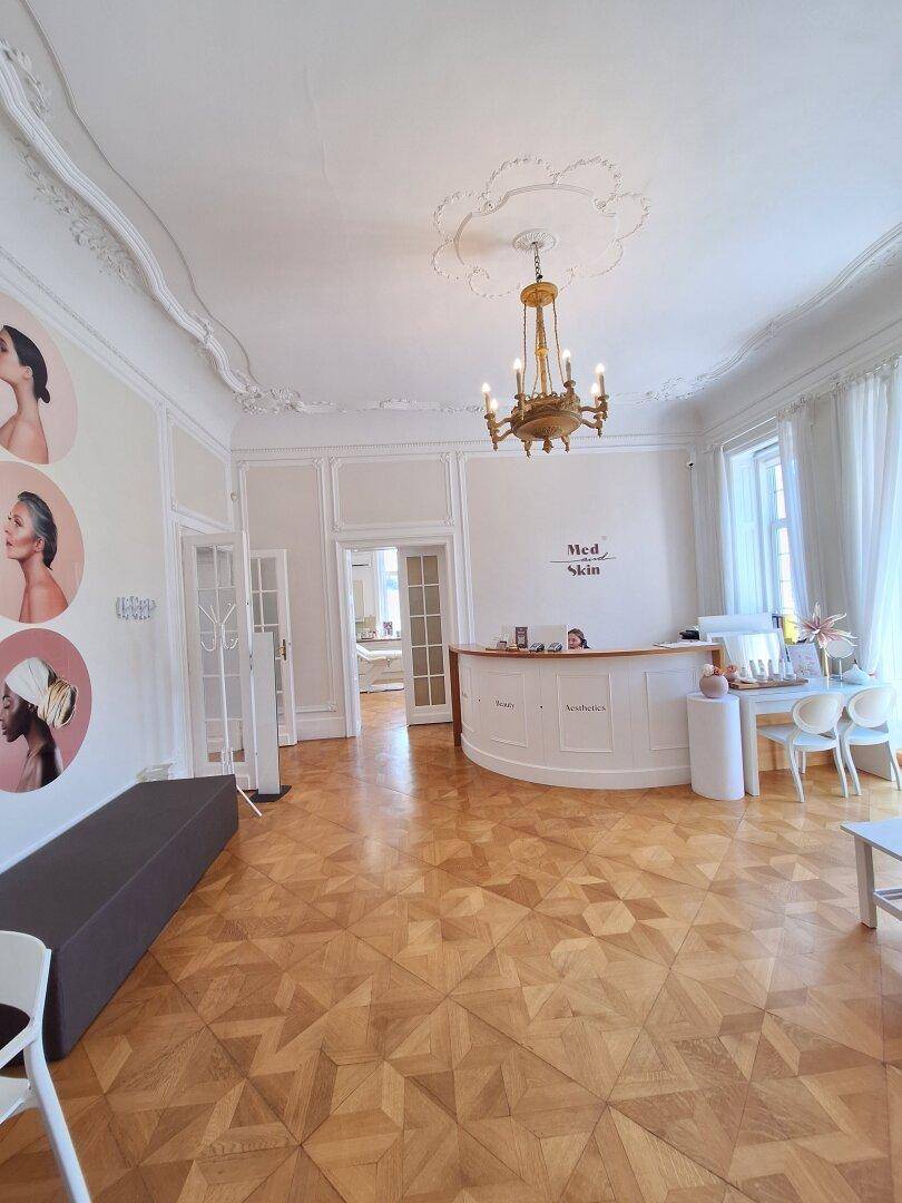 Heller Empfangsbereich mit elegantem Parkettboden, Stuckdecke und einer geschwungenen Rezeptionstheke.