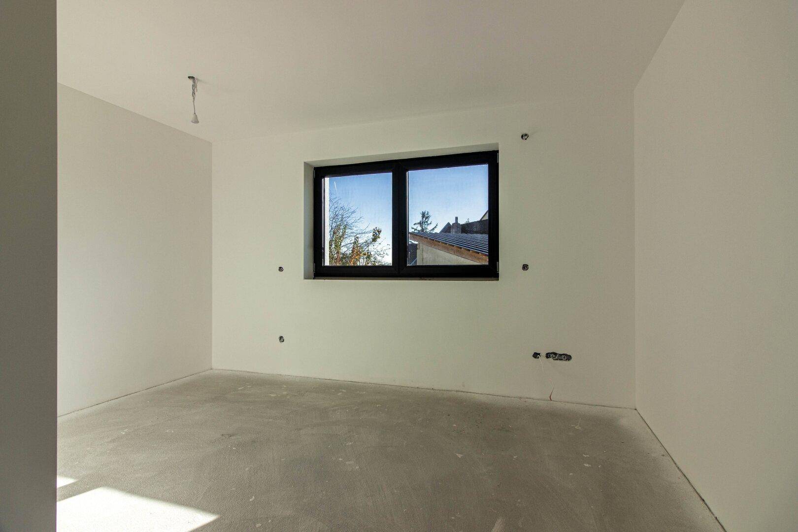 Unmöbliertes Schlafzimmer im Rohbau mit Betonboden und Fenster, bereit für den Innenausbau.