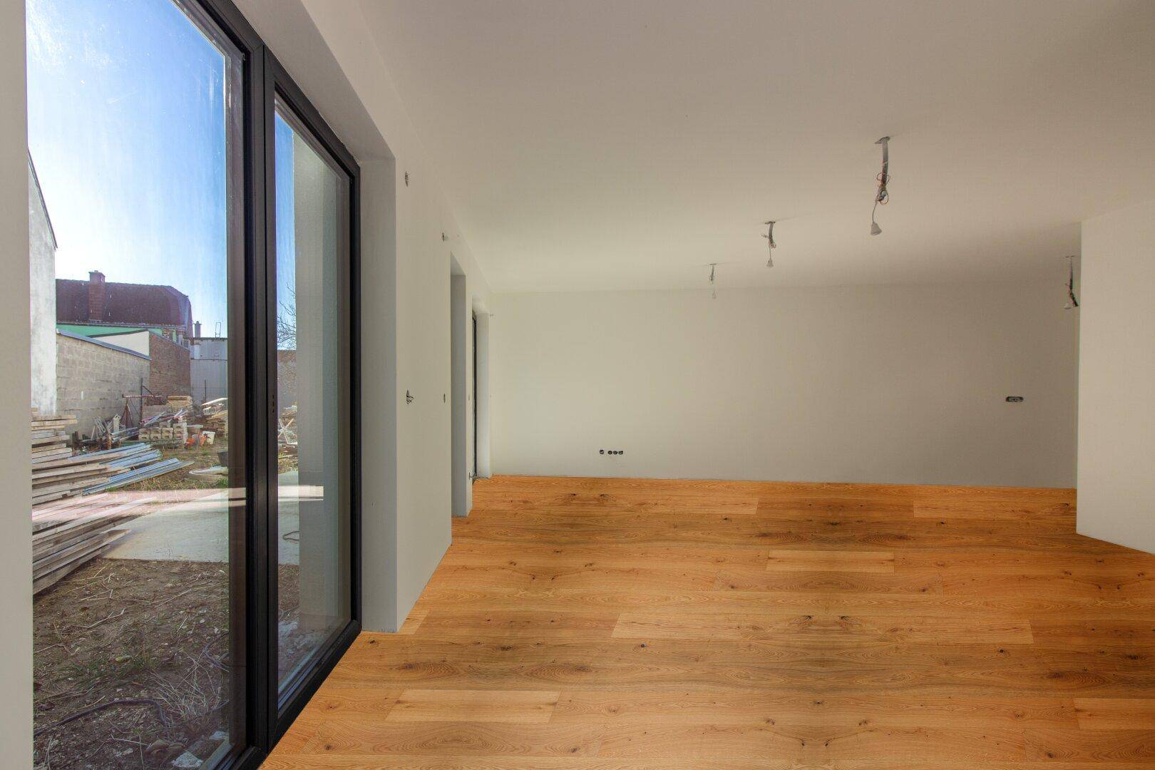Lichtdurchfluteter Raum mit neuem Holzparkett und bodentiefen Fenstern mit Blick ins Freie.