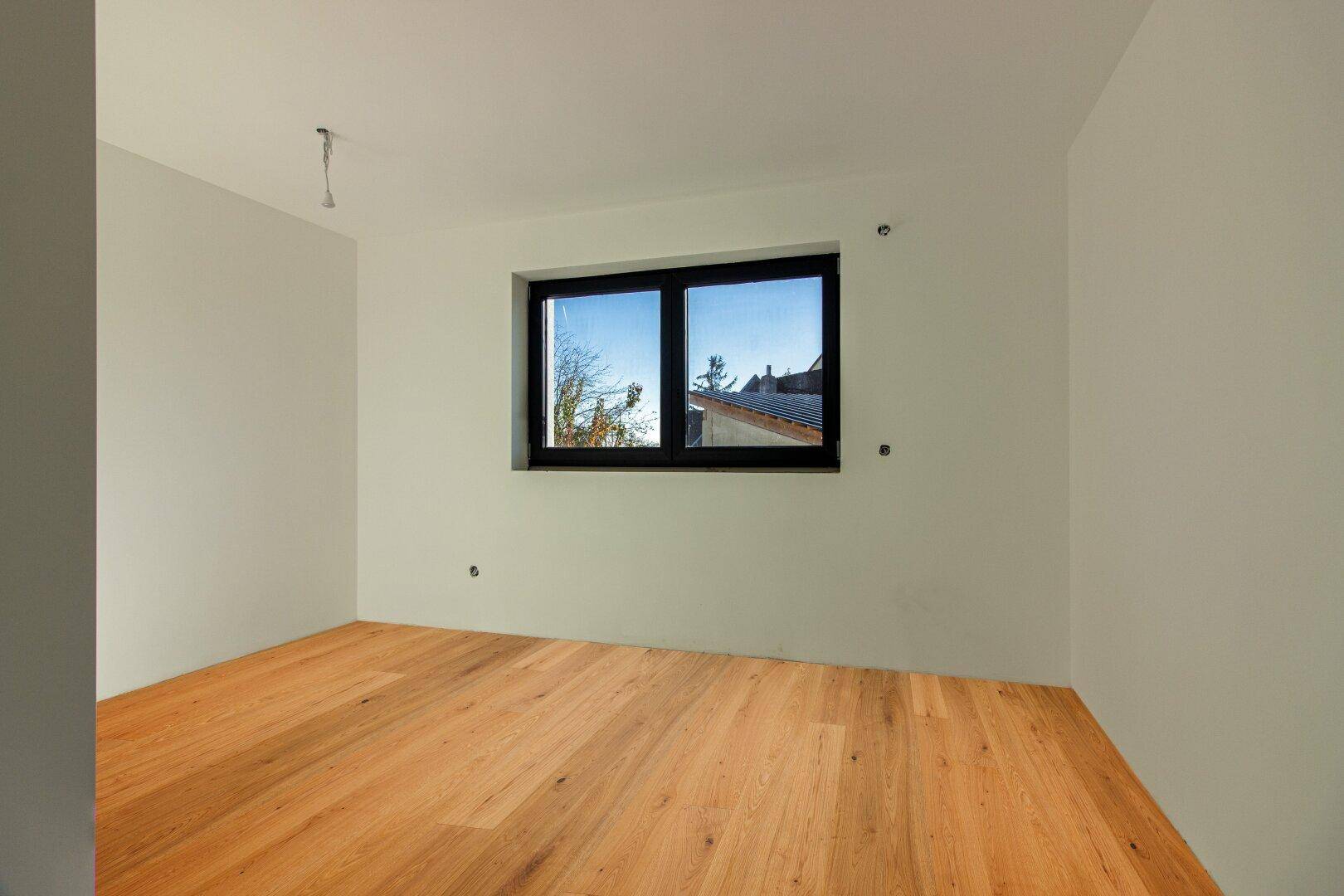 Helles Schlafzimmer mit neuem Holzparkett und Fenster, das einen Blick auf die Umgebung bietet.