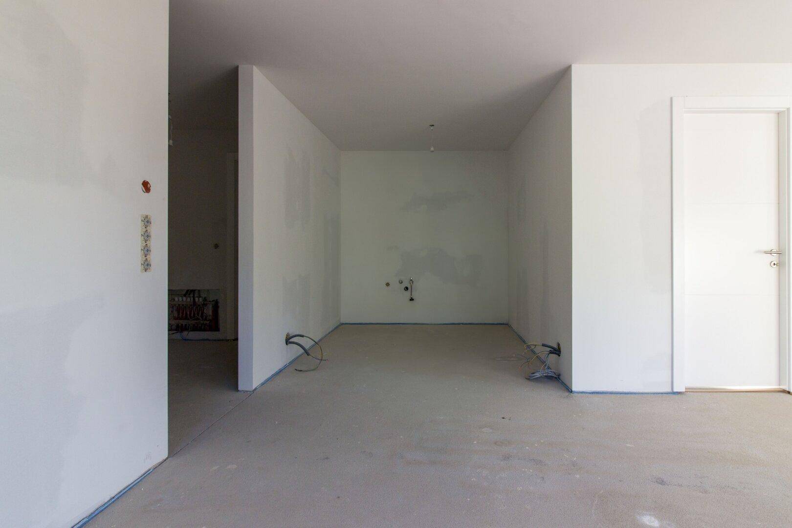 Unfertige Küche mit vorbereiteten Anschlüssen und Estrichboden, bereit für den Einbau.