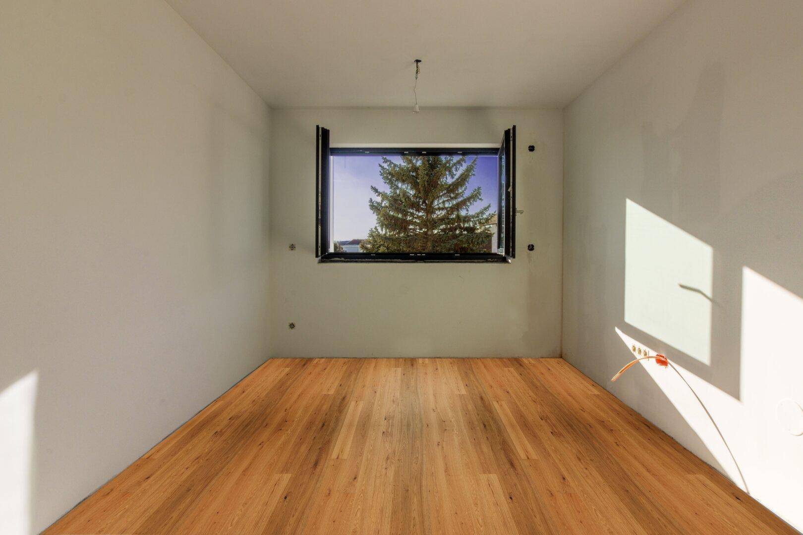 Heller Raum mit neuem Holzboden und großem Fenster mit Blick auf einen Baum.