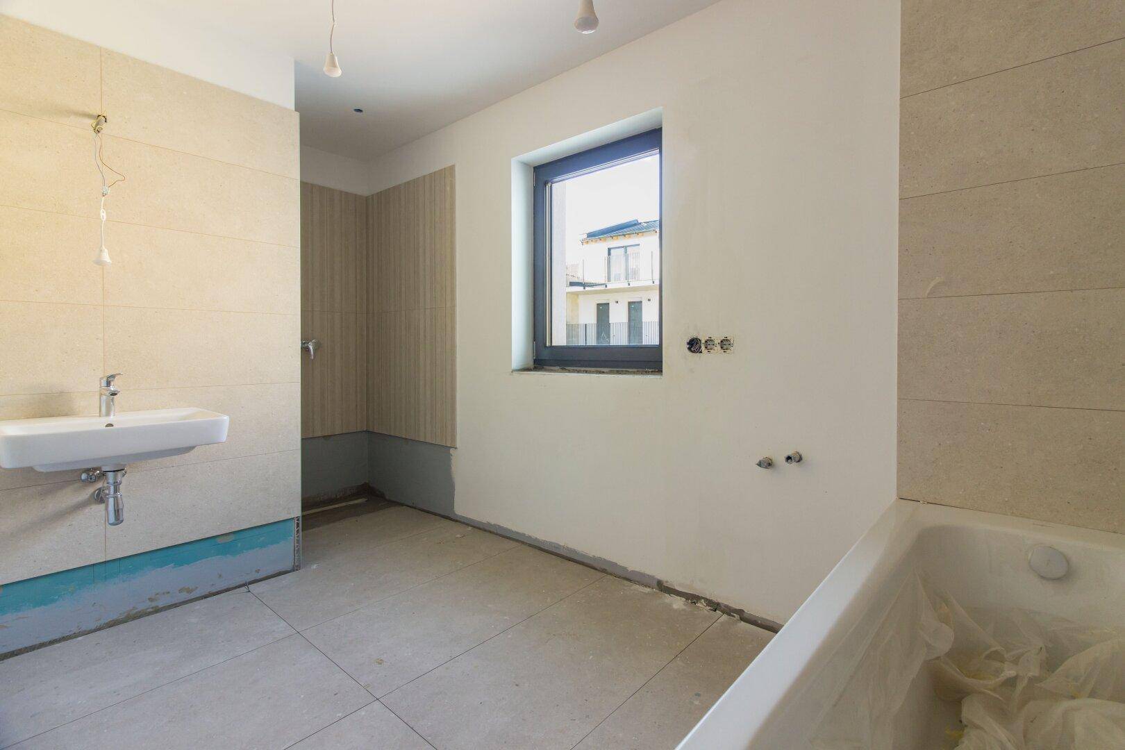 Badezimmer im Bau mit Badewanne, Waschbecken und Fliesen an den Wänden.