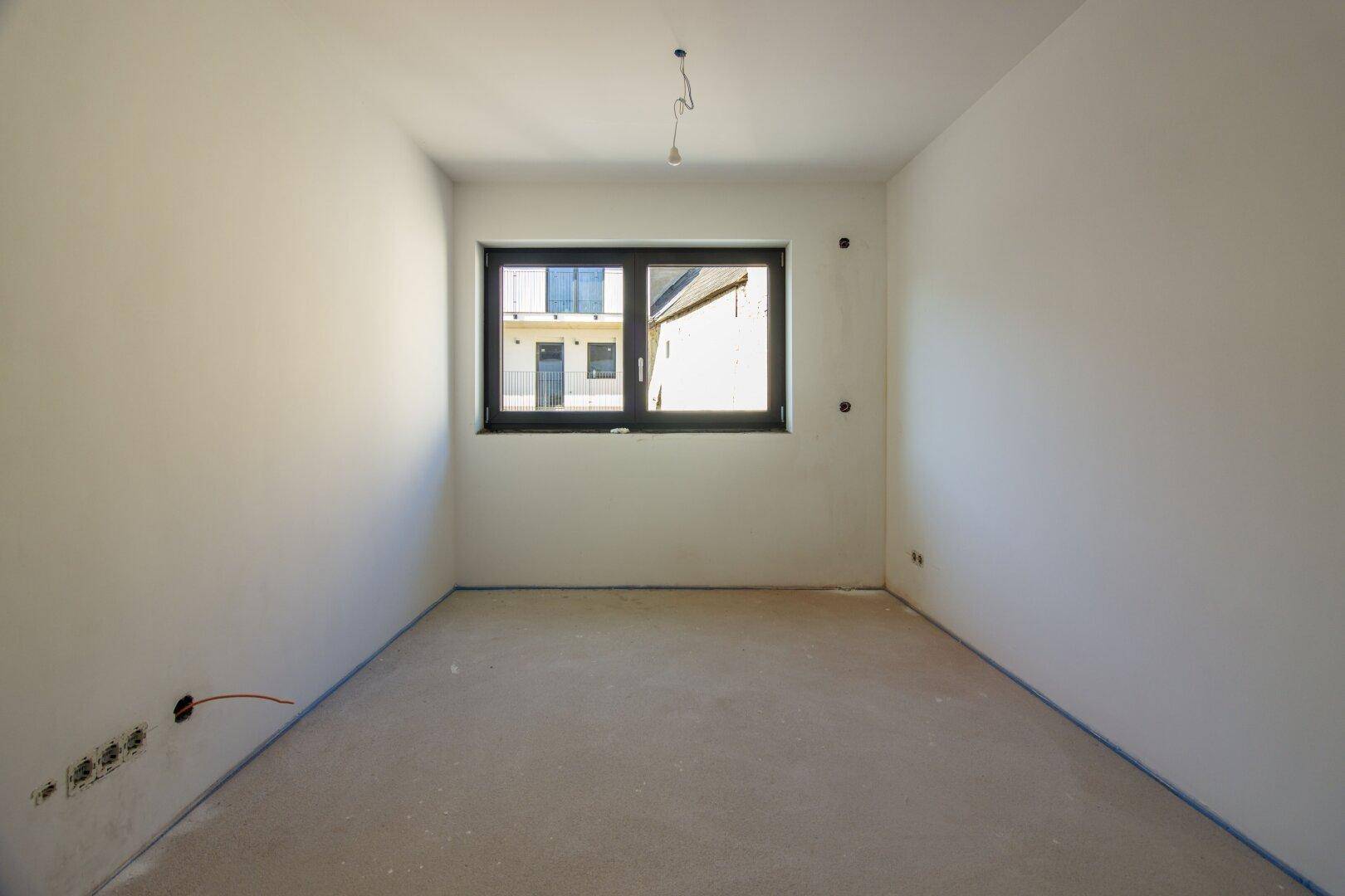 Unfertiger Raum mit Estrichboden und Fenster, bereit für die individuelle Gestaltung.