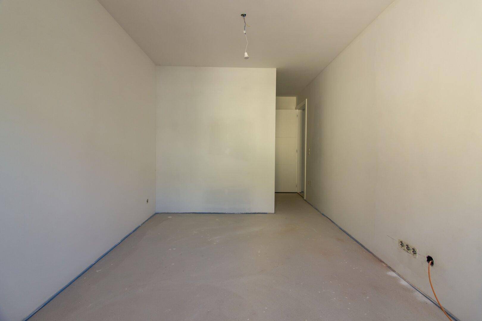 Unfertiger länglicher Raum mit Estrichboden und Türzugang, bereit für den Ausbau.