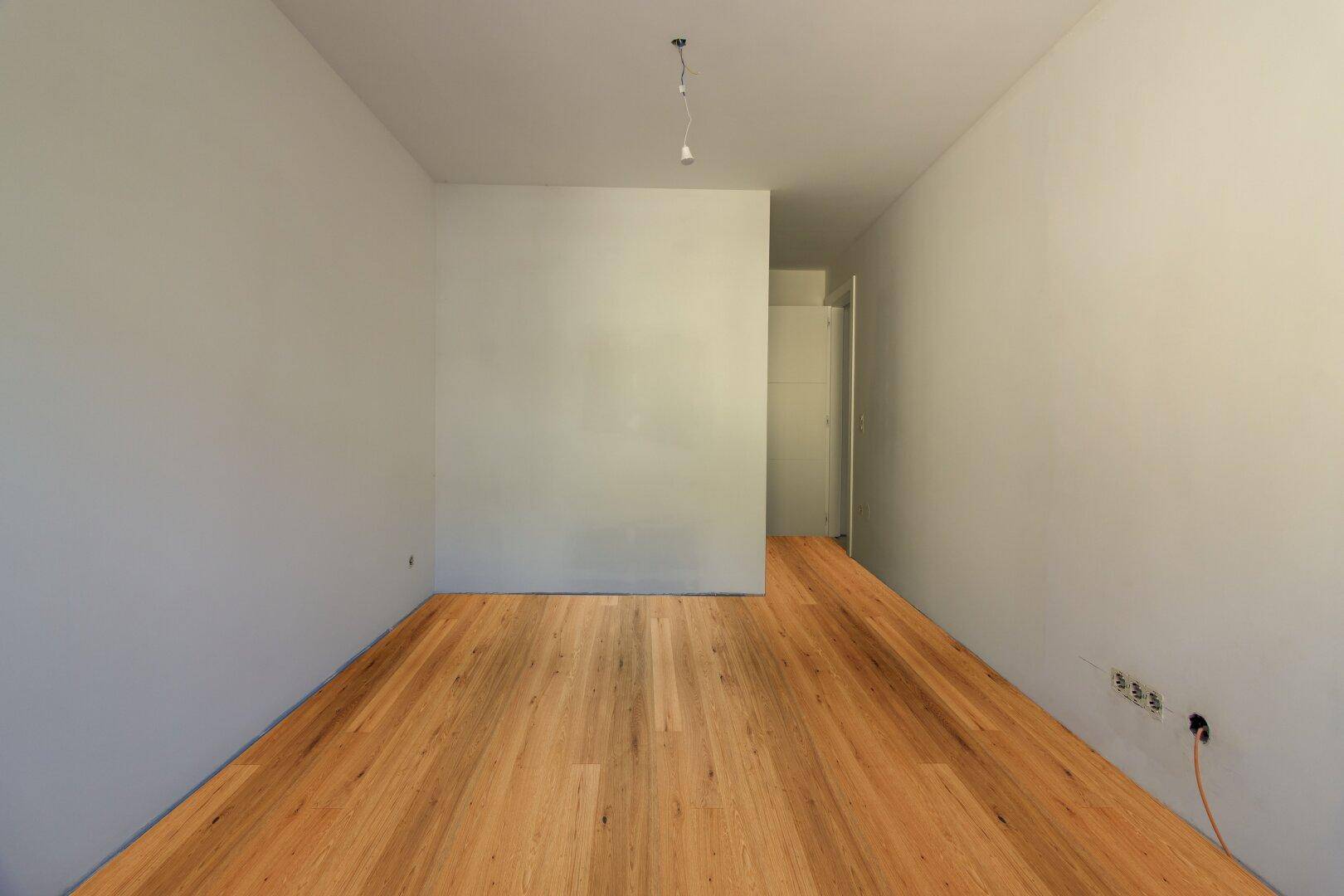 Länglicher Raum mit neuem Holzboden und Türzugang, geeignet als Schlaf- oder Arbeitszimmer.