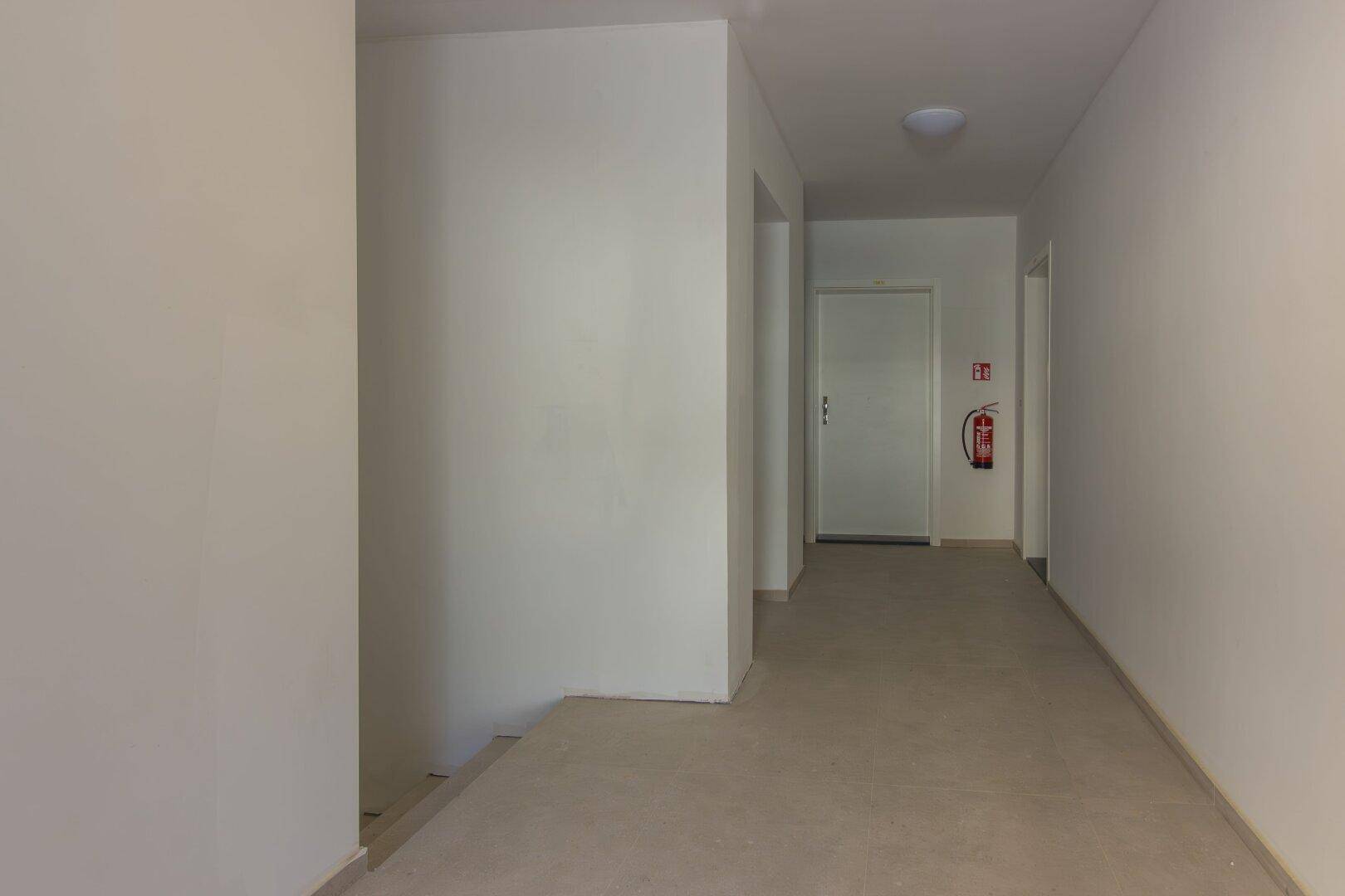 Heller Flur mit Estrichboden und Brandschutzvorrichtung, der zu weiteren Räumen führt.