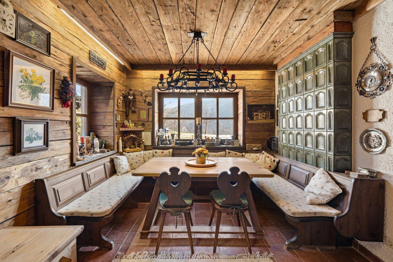 Gemütlicher Essbereich im alpinen Stil mit Kachelofen, Holzwänden und Blick auf die Berge.