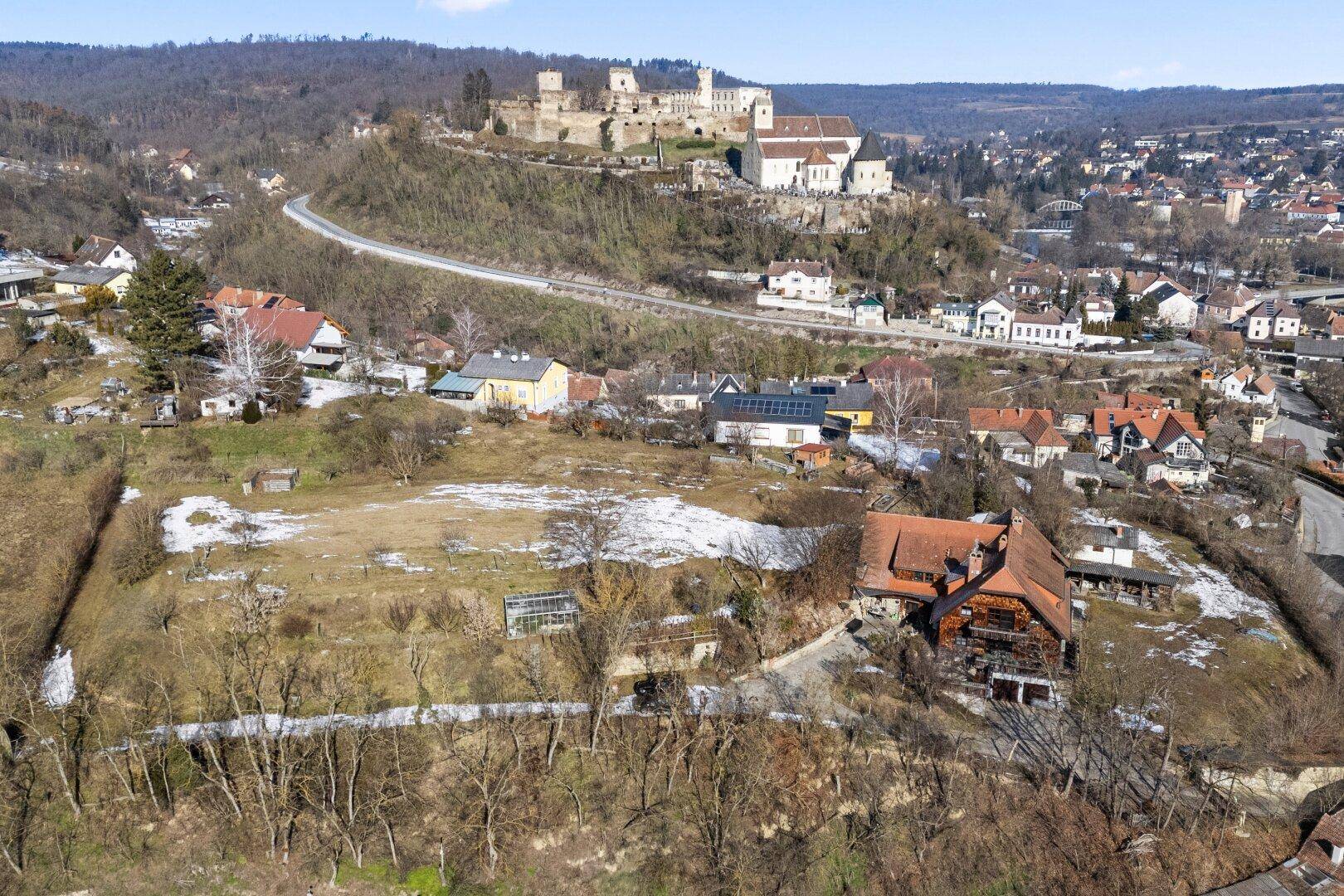 Weitläufige Luftaufnahme des Anwesens mit Haus und umliegender Landschaft, inklusive Burg im Hintergrund.